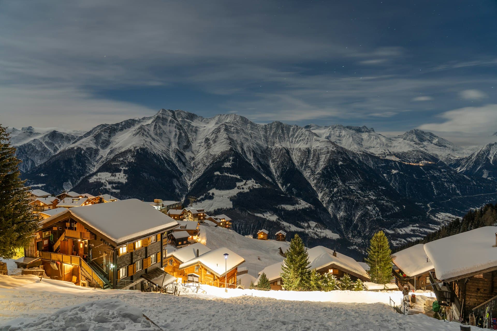 Holzchalets im Schnee vor einer Bergkette am Abend