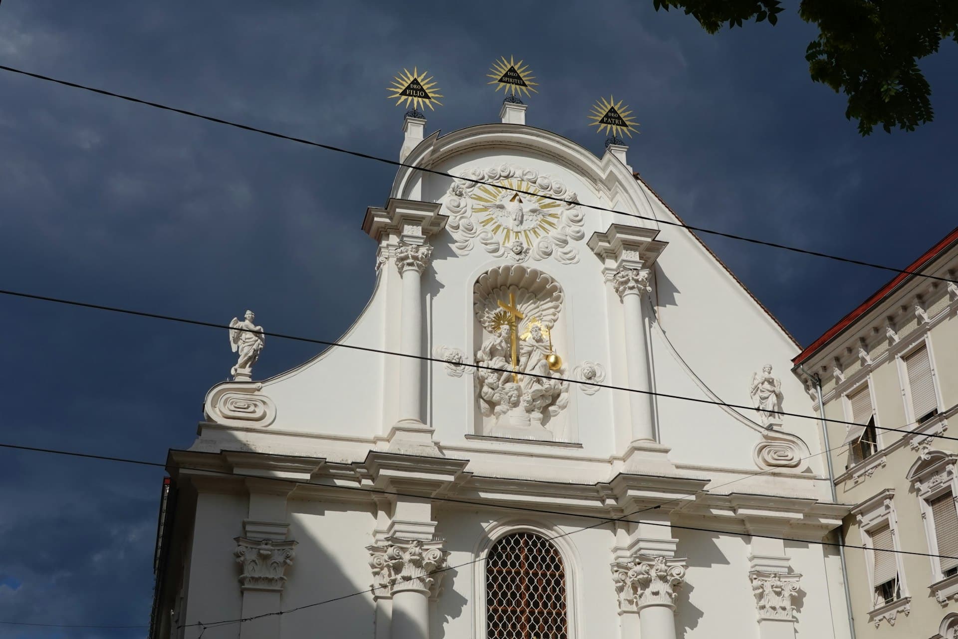 Weiße barocke Fassade mit goldenen Verzierungen vor dunklem Himmel