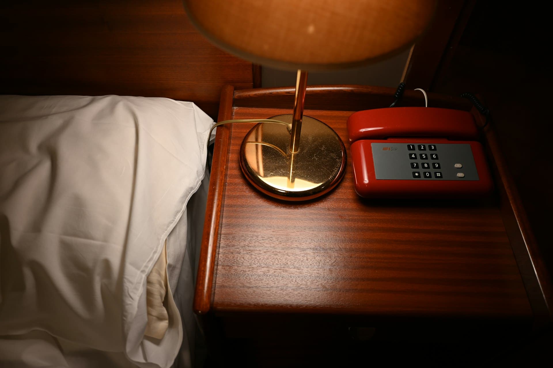 Nachttisch mit Lampe und rotem Telefon in einem Hotelzimmer