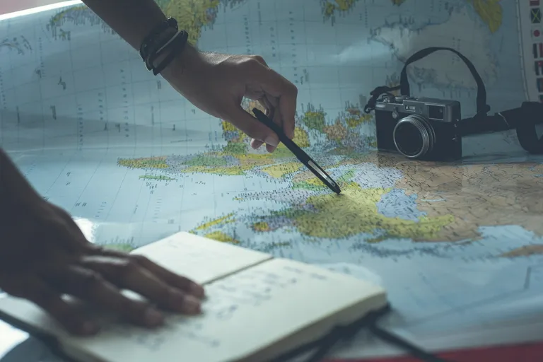 Hände planen eine Reise mit Landkarte und Notizbuch